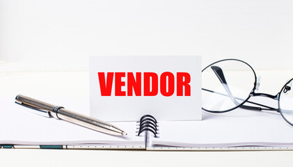 Close-up of a white card with the text VENDOR, a stylish pen and glasses on a desktop.