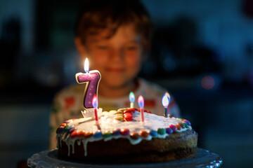Adorable happy blond little kid boy celebrating his birthday. Child blowing seven candles on...