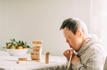 An elderly woman with down syndrome builds towers of wooden toy blocks