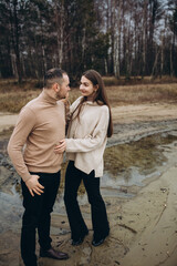 a man and a woman are walking along the shore of the lake, cold foggy weather. romantic photo in beige tones. holding a woman's hand, a love story. beige sweaters. romantic photos by the lake