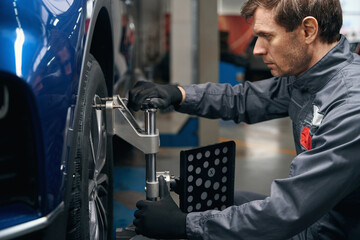 Professional male inspecting wheel alignment in the workshop