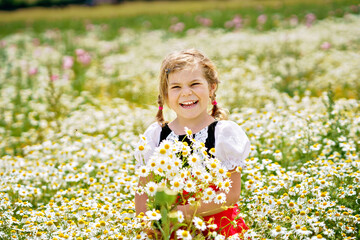 Little preschool girl in daisy flower field. Cute happy child in red riding hood dress play outdoor on blossom flowering meadow with daisies. Leisure activity in nature with children.