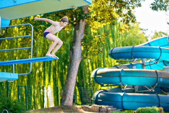 Active teenager boy jumping into an outdoor pool from spring board or 5 meters diving tower learning to dive during sport class on a hot summer day. Happy brave child.