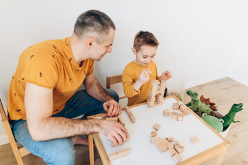 Loving dad and little boy child have fun play build construct with wooden blocks bricks. Father and son concept