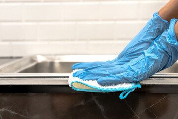 Close up housemaid with blue rubber gloves with towel cleaning kitchen sink, Hands Concept