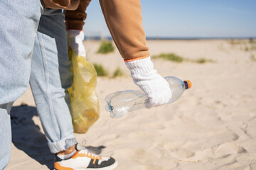 Young man collecting in plastic bag rubish and plastic bottles on the beach