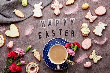 Happy Easter text with decorated Easter cookies, pink flowers, coffee cup and eggs flat lay.