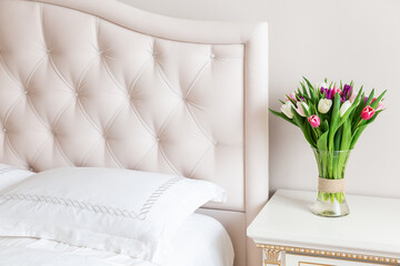 Bedroom in soft light colors. Vase of colorful tulips in light cozy bedroom interior.