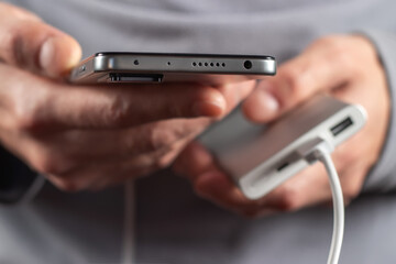 the man is holding the phone and the charger. Powerbank and smartphone in hand.