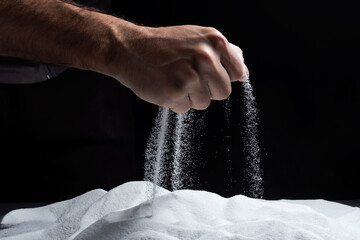 Man with handful of white dry sand in her hands, spilling sand through fingers on black background.