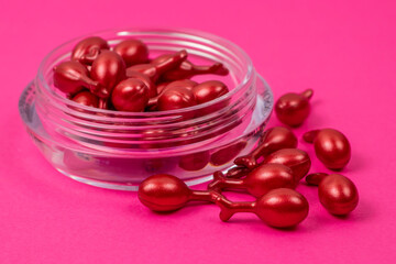 Red capsules with cosmetic oil for the face on pink background