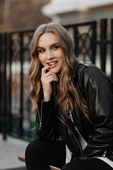 Fototapeta premium Close up portrait of a beautiful smiling young blonde woman in a black leather jacket on the a city street background