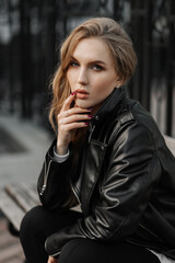Close up portrait of a beautiful smiling young blonde woman in a black leather jacket on the  a city street background