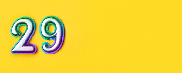 29 years celebration. Banner with birthday greetings. Multi colored metal number twenty nine on a yellow background. Copy space, top view.
