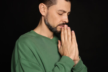 Man with clasped hands praying on black background