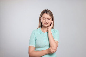 Obraz premium Young woman suffering from ear pain on light grey background