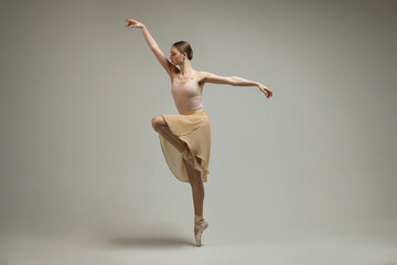 Obraz na płótnie Canvas Young ballerina practicing dance moves on grey background
