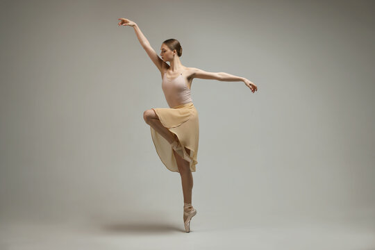 Young ballerina practicing dance moves on grey background
