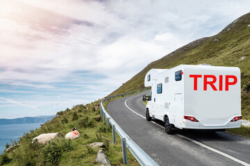 White motorhome with sign trip moving on a small mountain road and beautiful country side with ocean in foreground. Low cloudy sky. Travel with camper concept. Trip to nature.