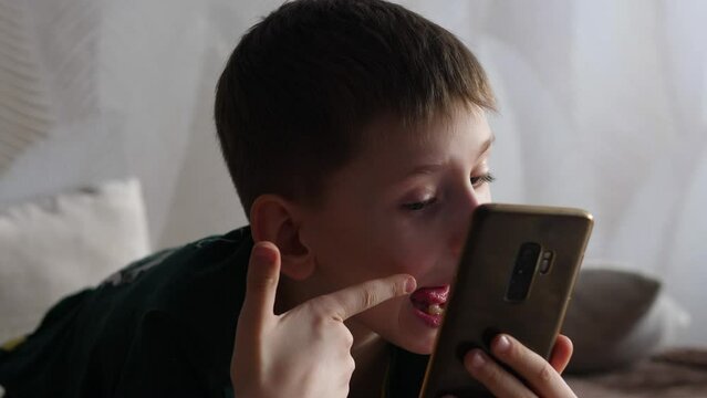 portrait of a caucasian boy 8-9 years old showing grimaces in front of a smartphone camera while being inside. the child poses in front of the phone making funny facial expressions for a selfie.
