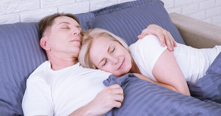 Calm couple sleeping and spooning in bed in bedroom at home.