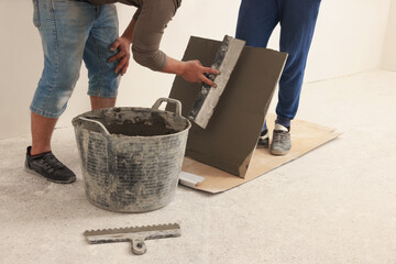 Worker spreading adhesive mix over tile with spatula, closeup