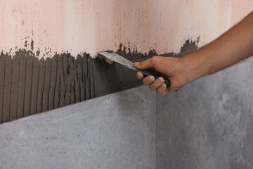 Worker spreading adhesive mix on wall, closeup. Tiles installation process