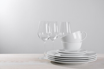 Fototapeta na wymiar Set of clean dishware and glasses on white wooden table against light background. Space for text
