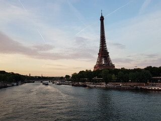 Fototapeta premium Classic Paris view with Eiffel Tower, Seine, boats and trees with vapor trails and clouds on the sky before sunset