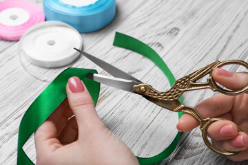 Woman cutting green ribbon with scissors at white wooden table, closeup