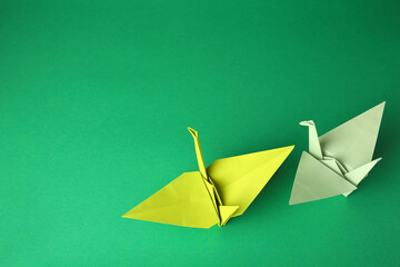 Colorful paper origami cranes on green background, flat lay. Space for text