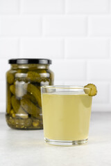 Pickle juice or brine in a glass and jar of pickled cucumbers on a white background. Copy Space.