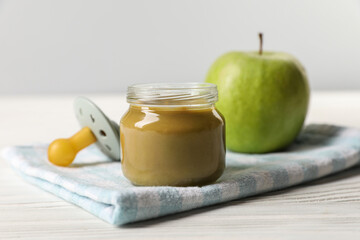 Jar with healthy baby food, apple and pacifier on white wooden table