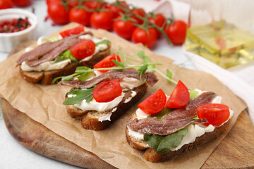 Delicious bruschettas with anchovies, tomatoes, microgreens and cream cheese on white table, closeup