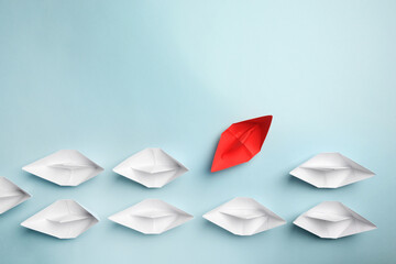 Red paper boat floating away from others on light background, flat lay with space for text....