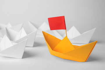 Group of paper boats following orange one on white background, closeup. Leadership concept