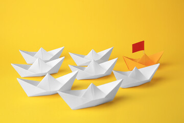 Group of paper boats following yellow one on color background. Leadership concept