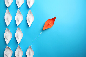 Orange paper boat floating away from others on light blue background, flat lay with space for text....