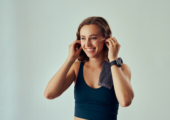 Happy young caucasian woman in sports bra looking away while putting in wireless headphones