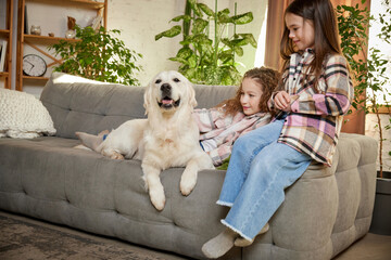 Two little cute happy girls, sisters sitting at home and playing with Golden retriever dog....