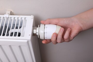 Girl adjusting heating radiator thermostat near white wall indoors, closeup