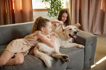 Beautiful purebreed dog, sand color American retriver lying on sofa with two kids, little girls in casual style clothes. Concept of happiness, family, care, animal and vet