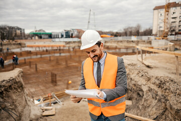 A happy site chief is standing on reconstruction area and checking on paperwork.