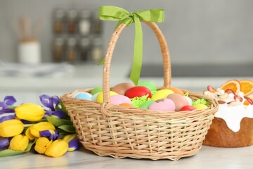 Easter basket with painted eggs between tulips and cake on white marble table indoors
