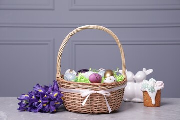 Fototapeta na wymiar Easter basket with many painted eggs near tasty cake, flowers and figure of rabbits on grey textured table