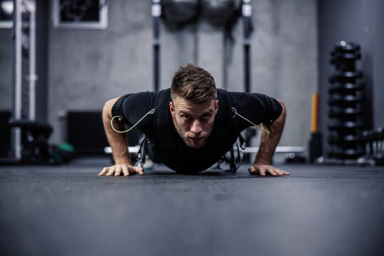A male fitness instructor in a special department for EMS technology does push-ups and arm exercises in a modern gym concept. Revolution in training, body rehabilitation. Copy space for ads massage
