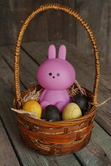 Bunny or rabbit and colorful Esther's eggs in the basket. Adorable small pink rabbit and Esther's eggs on wood background. Rabit standing