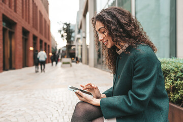 Young woman with curly hair using her smartphone in the city