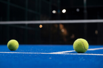 two balls on the surface of a blue paddle tennis court at night