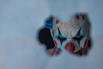 Close-up of a creepy clown looking through a hole. The face of a man wearing a creepy clown mask,...